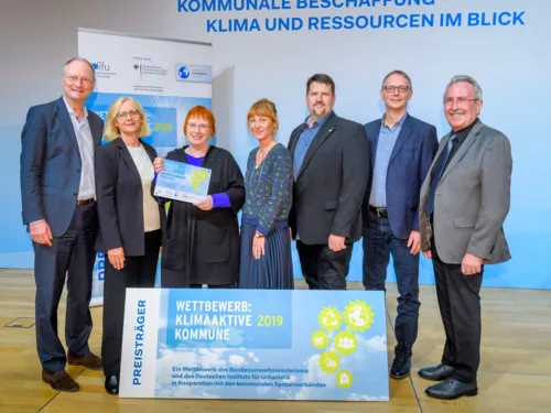 Sieben Personen stehen im Rahmen einer Preisverleihung vor einer blauen Wand und schauen in die Kamera